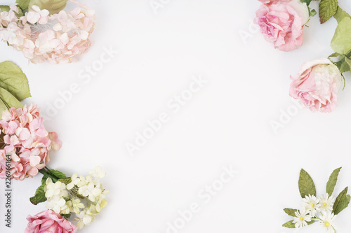 Frame made of pink and beige roses, hydrangea, green leaves, branches on white background. Flat lay, top view. Wedding's background. Valentine's background with copy space.
