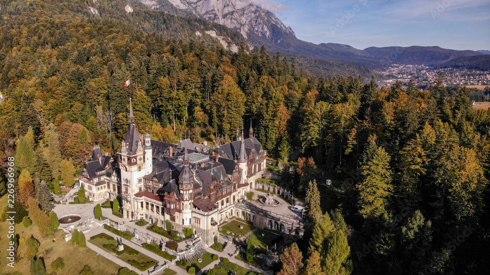 Aerial view of Peles Castle in Sinaia, Carpathian mountains, Brasov region, Romania. Beautiful autumn landscape in castle surrounded with the forest and high mountains.