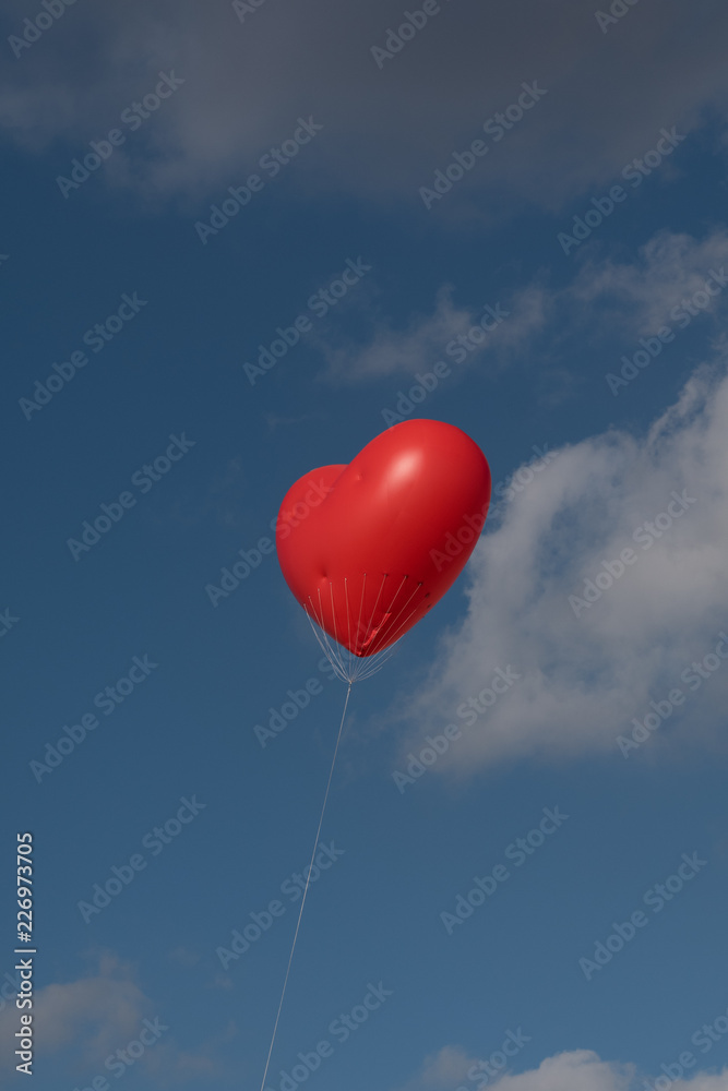 Fototapeta premium red heart balloon in front of blue cloudy sky 