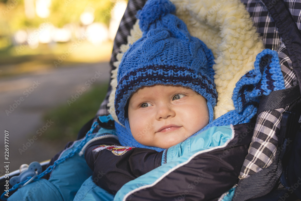 A small child in a hat and scarf sitting in a stroller A small child in a hat and scarf sitting in a stroller