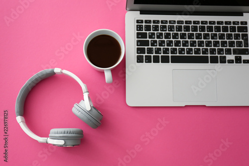 Headphones with laptop and cup of coffee on color table