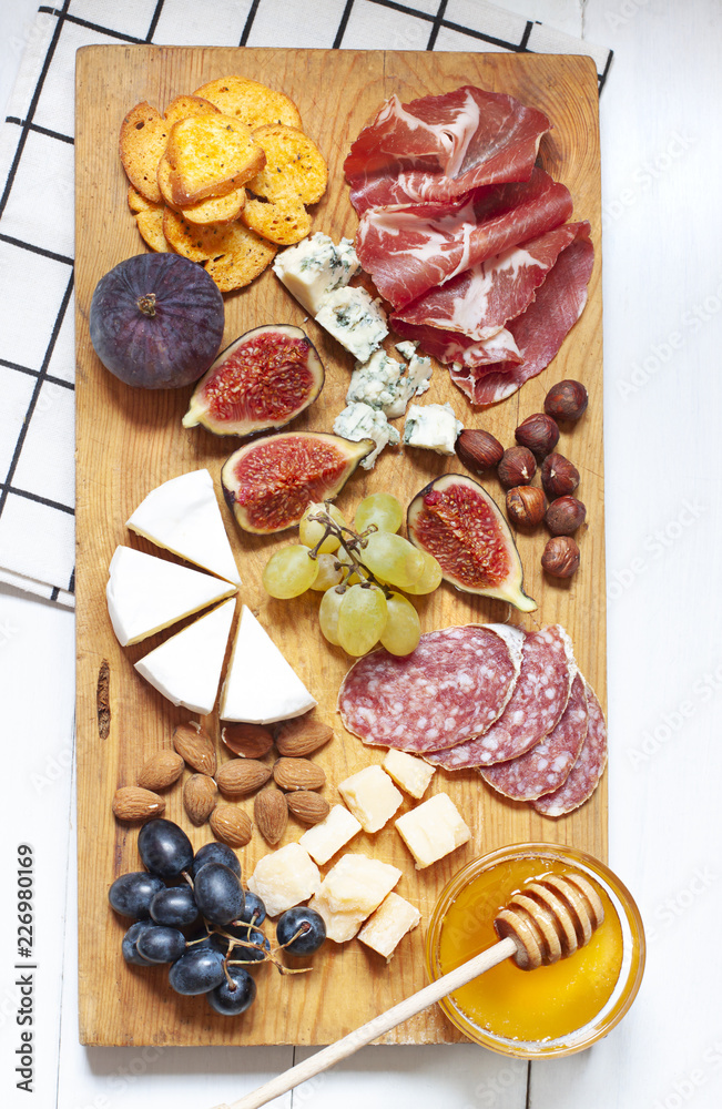 Antipasti food white flat lay with nuts, honey, cured meat, salami, cheeses, grapes and figs on the wooden board. Top view snack concept composition Antipasti food white flat lay with nuts, honey, cured meat, salami, cheeses, grapes and figs on the wooden board. Top view snack concept composition