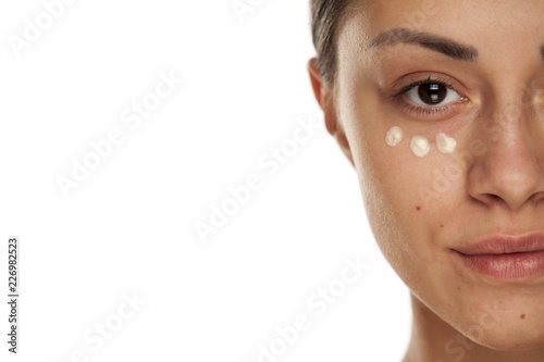 beautiful young woman with moisturizer on her face on white background