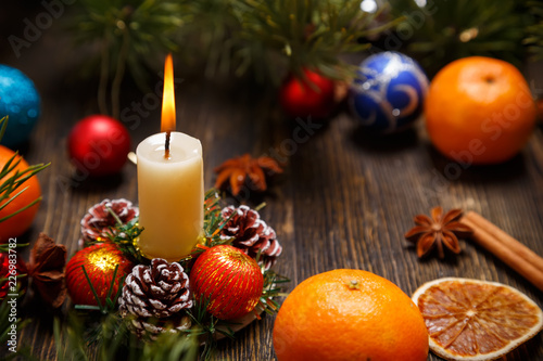Christmas decoration with the burning candle, tangerines, pine cones and balls on a wooden table, a copy space for your own text.