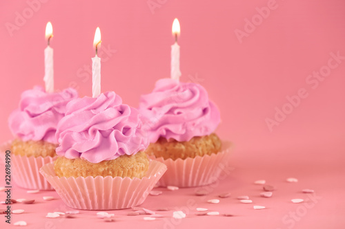 Delicious birthday cupcakes with burning candles on color background