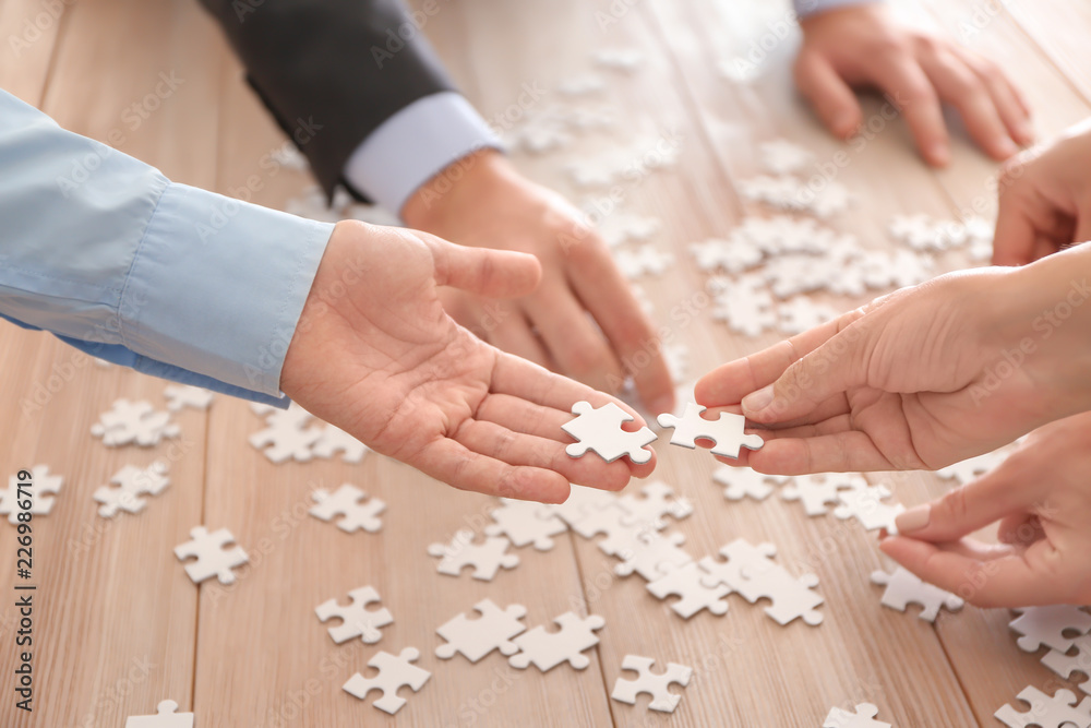 Business team assembling puzzle on wooden table Business team assembling puzzle on wooden table