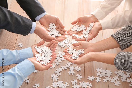 Business team holding pieces of puzzle over wooden table, closeup