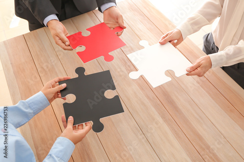 Business team holding pieces of puzzle over wooden table photo