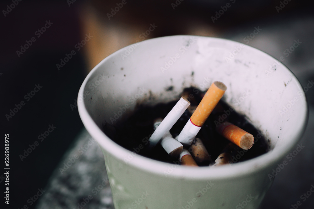 Burning cigarettes in ashtray on background. Area for smoking have cigarette stub on paper cup. Burning cigarettes in ashtray on background. Area for smoking have cigarette stub on paper cup.