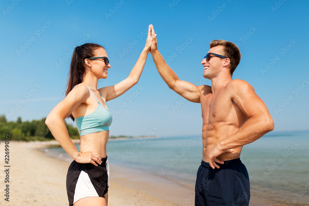 fitness, sport and lifestyle concept - happy couple in sports clothes and sunglasses on beach making high five gesture fitness, sport and lifestyle concept - happy couple in sports clothes and sunglasses on beach making high five gesture