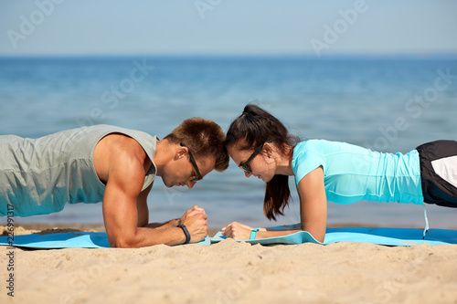 fitness, sport and lifestyle concept - couple doing plank exercise on summer beach