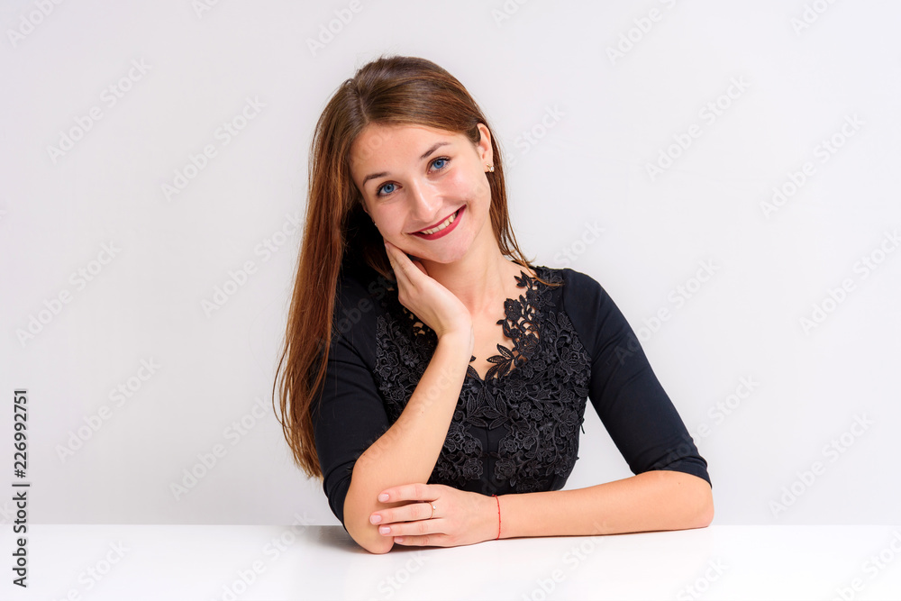 Studio portrait of a beautiful brunette girl on a white background sitting at the table shows different emotions. Studio portrait of a beautiful brunette girl on a white background sitting at the table shows different emotions.