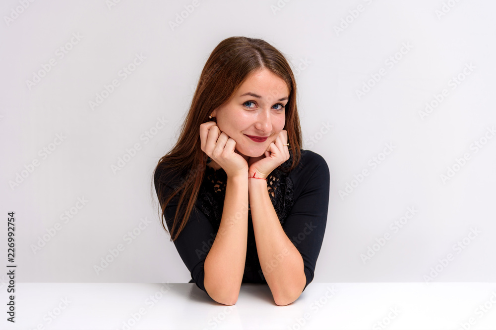 Studio portrait of a beautiful brunette girl on a white background sitting at the table shows different emotions. Studio portrait of a beautiful brunette girl on a white background sitting at the table shows different emotions.
