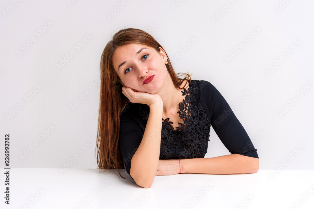 Studio portrait of a beautiful brunette girl on a white background sitting at the table shows different emotions. Studio portrait of a beautiful brunette girl on a white background sitting at the table shows different emotions.