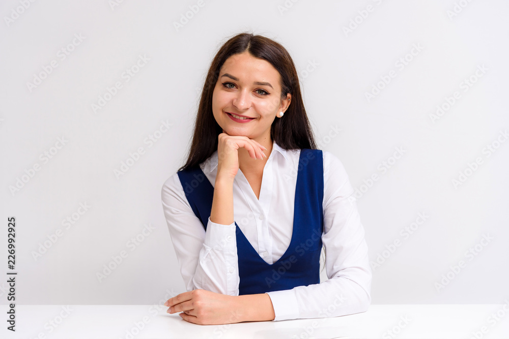 Studio portrait of a beautiful brunette girl on a white background sitting at the table shows different emotions. Studio portrait of a beautiful brunette girl on a white background sitting at the table shows different emotions.