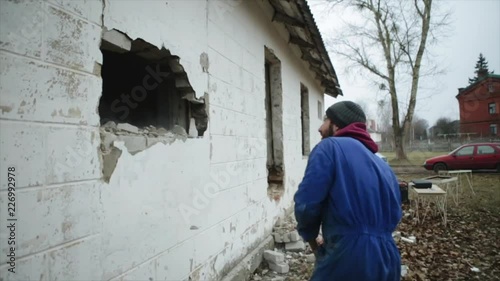 Slow motion. A worker with a hammer ruining an outside wall. Another man with a perforator working in the background. Falling bricks. Demolition work. Rearrangement photo