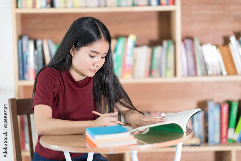 Cheerful girl sitting by wooden table and Reading book in library. Cheerful girl sitting by wooden table and Reading book in library.
