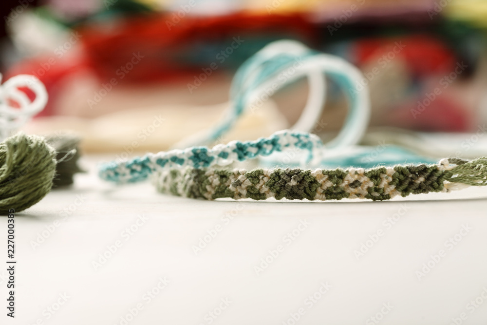 Handcrafted friendship bracelets on a white table with different colored threads Handcrafted friendship bracelets on a white table with different colored threads