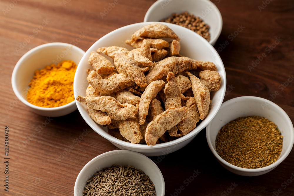 Raw dry soya meat chunks in a white bowl on a wooden table with different species Raw dry soya meat chunks in a white bowl on a wooden table with different species