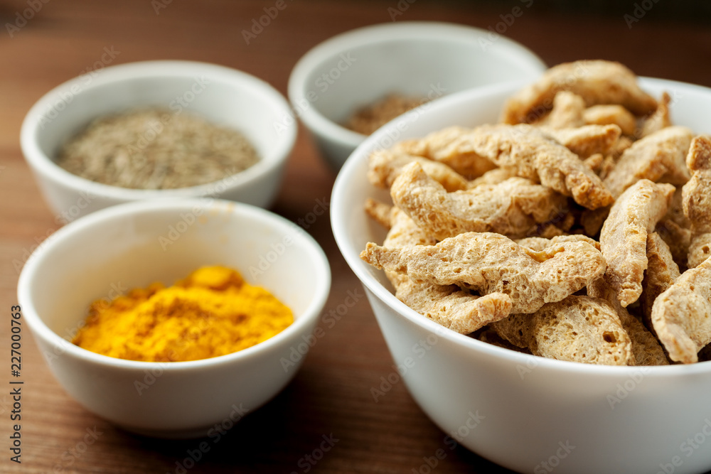 Raw dry soya meat chunks in a white bowl on a wooden table with different species Raw dry soya meat chunks in a white bowl on a wooden table with different species
