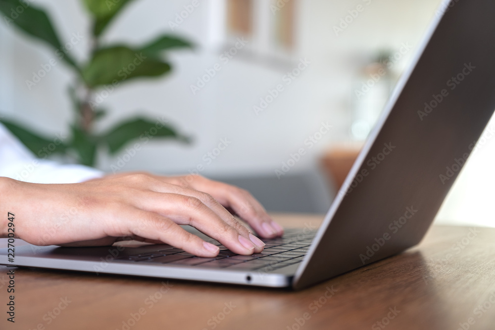 Closeup image of woman's hands using and typing on laptop keyboard on wooden table in office Closeup image of woman's hands using and typing on laptop keyboard on wooden table in office