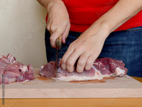 Fototapeta Naklejka Na Ścianę i Meble -  Close up of women hands cutting meat into pieces with knife on a wooden chopping board for making minced meat