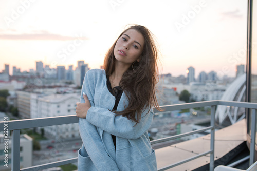 Attractive young woman stands against city and sunset.