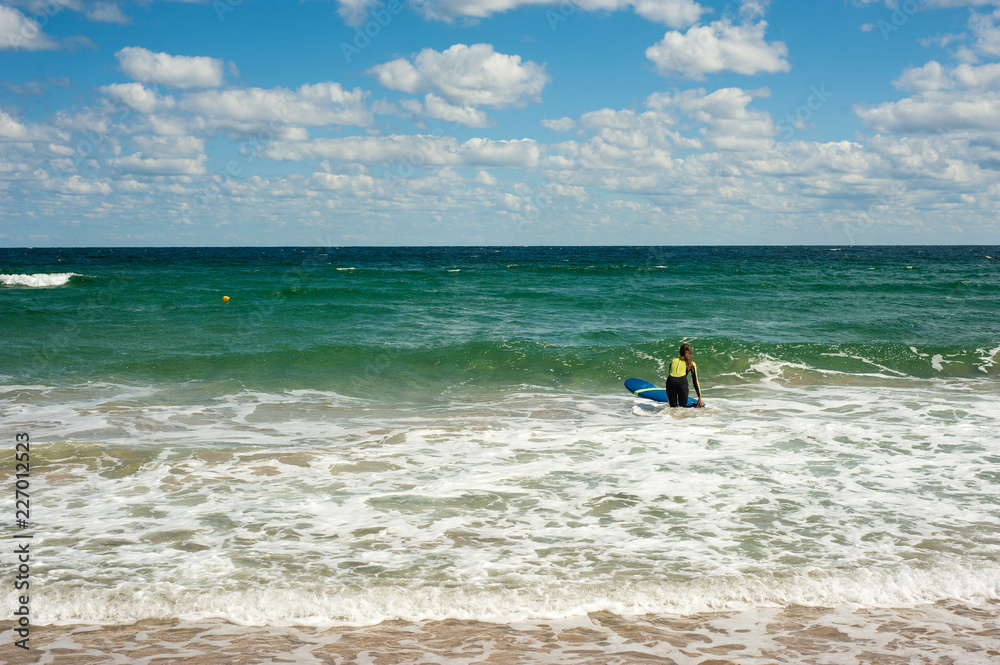 Girl learns to ride a surfboard on the sea in summer. Riding on a surfboard on the waves in a beautiful place. Surfer school on the beach.