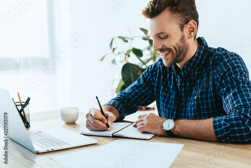 smiling businessman taking part in webinar at tabletop with laptop in office