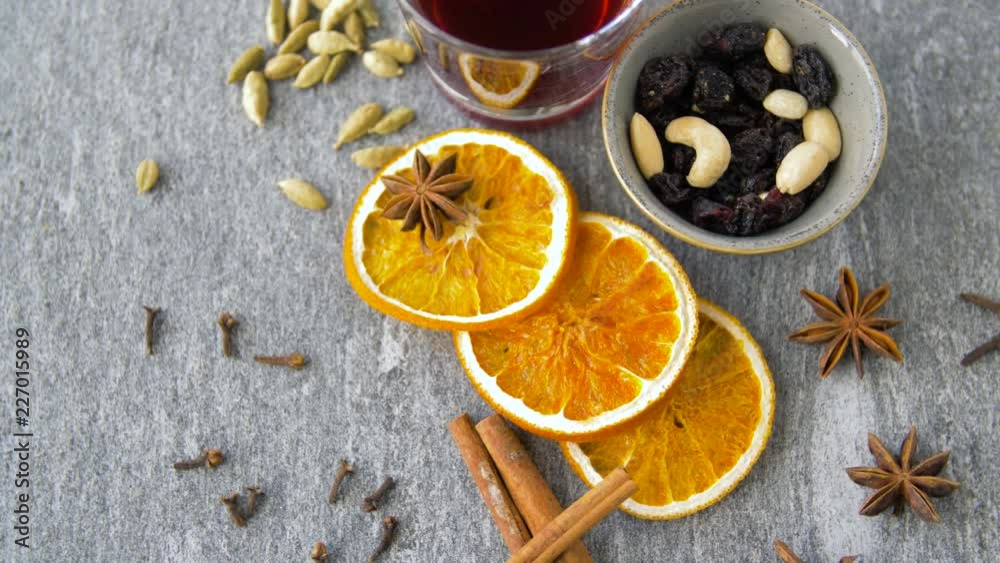 christmas and seasonal drinks concept - hot mulled wine, orange slices, raisins with cashew nuts and aromatic spices on grey background christmas and seasonal drinks concept - hot mulled wine, orange slices, raisins with cashew nuts and aromatic spices on grey background