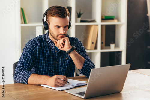 Фотография portrait of concentrated man in headphones taking part in webinar at tabletop wi