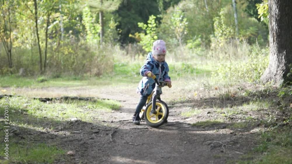A toddler is riding a downhill from a small forest slide. It is cold outside. The girl fun kicks and approaches the camera A toddler is riding a downhill from a small forest slide. It is cold outside. The girl fun kicks and approaches the camera