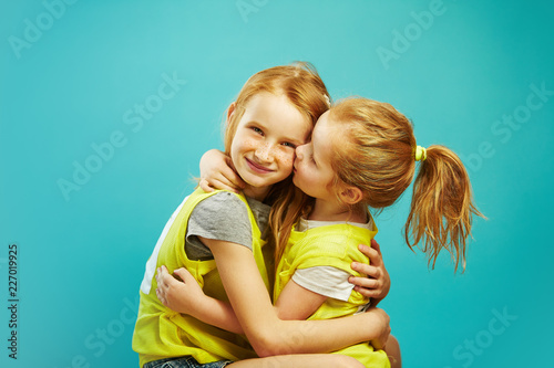 Little girl kissing her older sister on blue background.