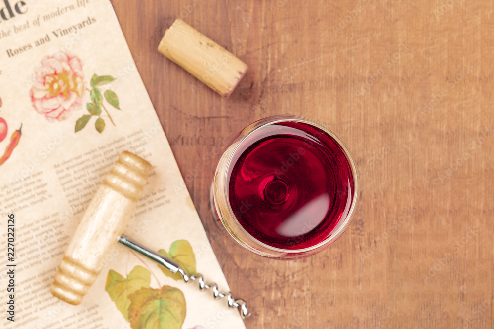 An overhead photo of a glass of red wine with a vintage corkscrew and a cork, shot on a blurred vintage newspaper An overhead photo of a glass of red wine with a vintage corkscrew and a cork, shot on a blurred vintage newspaper