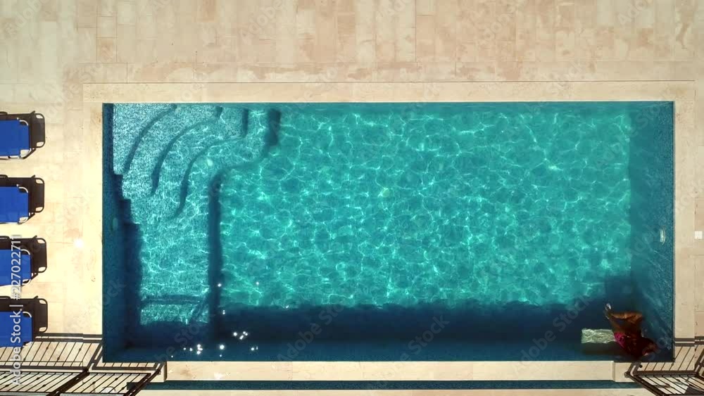 Aerial view of young girl jumping into swimming pool with inflatable pink ring. Aerial view of young girl jumping into swimming pool with inflatable pink ring.