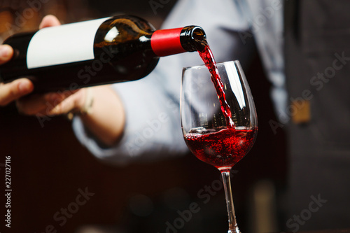 Waiter pouring red wine into wineglass. Sommelier pours alcoholic drink
