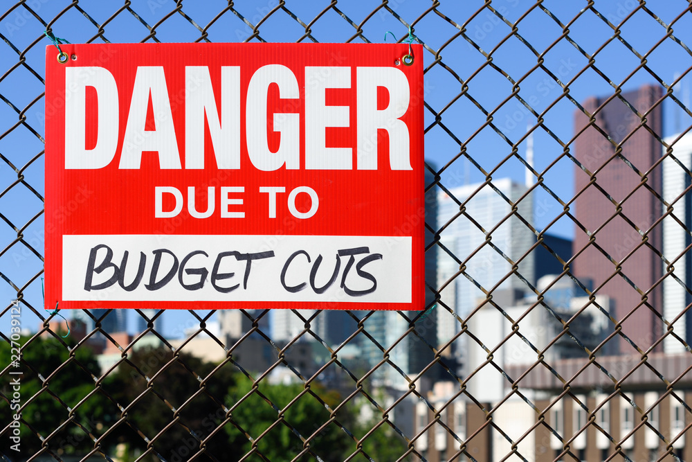 Sign danger due to budget cuts hanging on the fence Sign danger due to budget cuts hanging on the fence