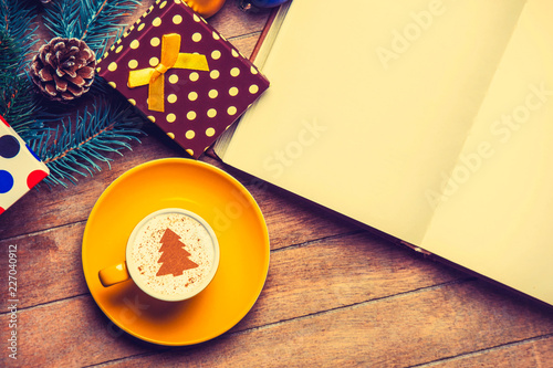 yellow cup of Cappuccino with cream Christmas tree and open book on wooden table near toys.