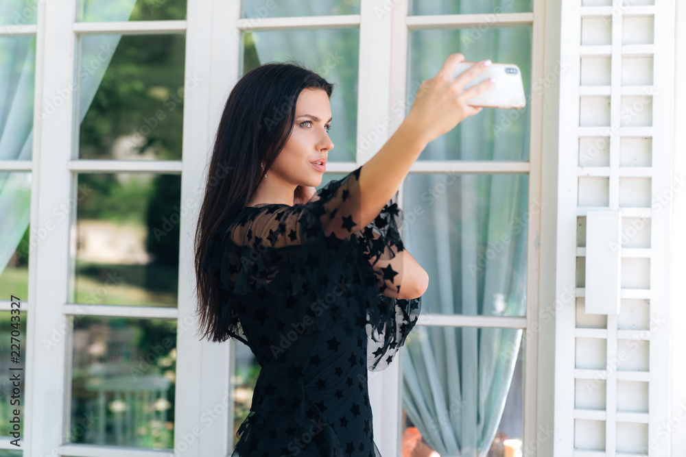 Fototapeta premium Fashionable beautiful young European girl makes selfie on her smartphone. Concept photo, gadgets, people, technology.