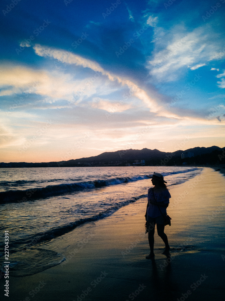 Fototapeta premium Woman walking along beach at sunset