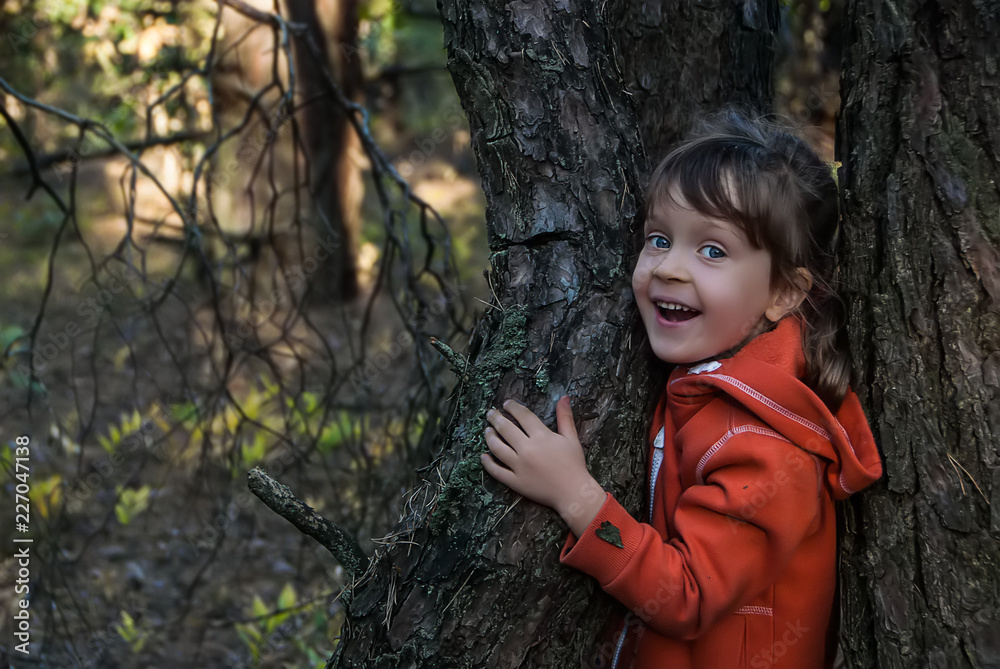 Laughing five-years-old girl stands between two trees in autumn forest and looks happy. Concept - happy and healthy childhood. Laughing five-years-old girl stands between two trees in autumn forest and looks happy. Concept - happy and healthy childhood.