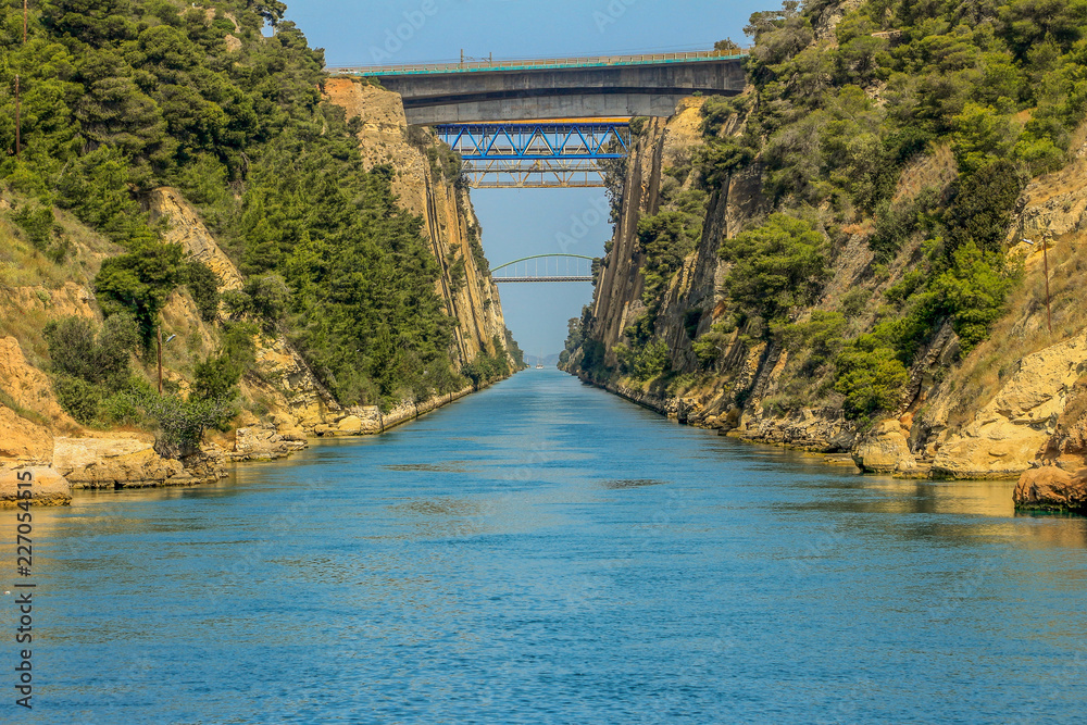 View of the historic Corinth Canal, Greece, going to the Ionian Sea, including a bridge above the canal and incredibly blue water.