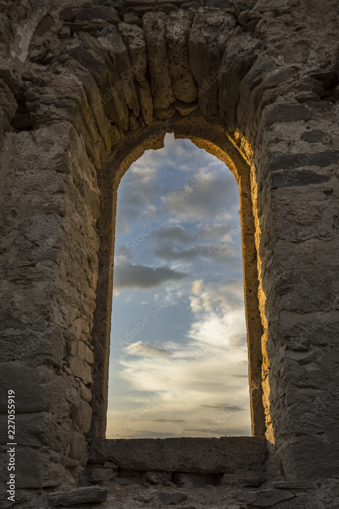 Beautiful colorful clouds on blue sky on sunset. View through arched window in old stone abandoned church. Аrchitecture concept.