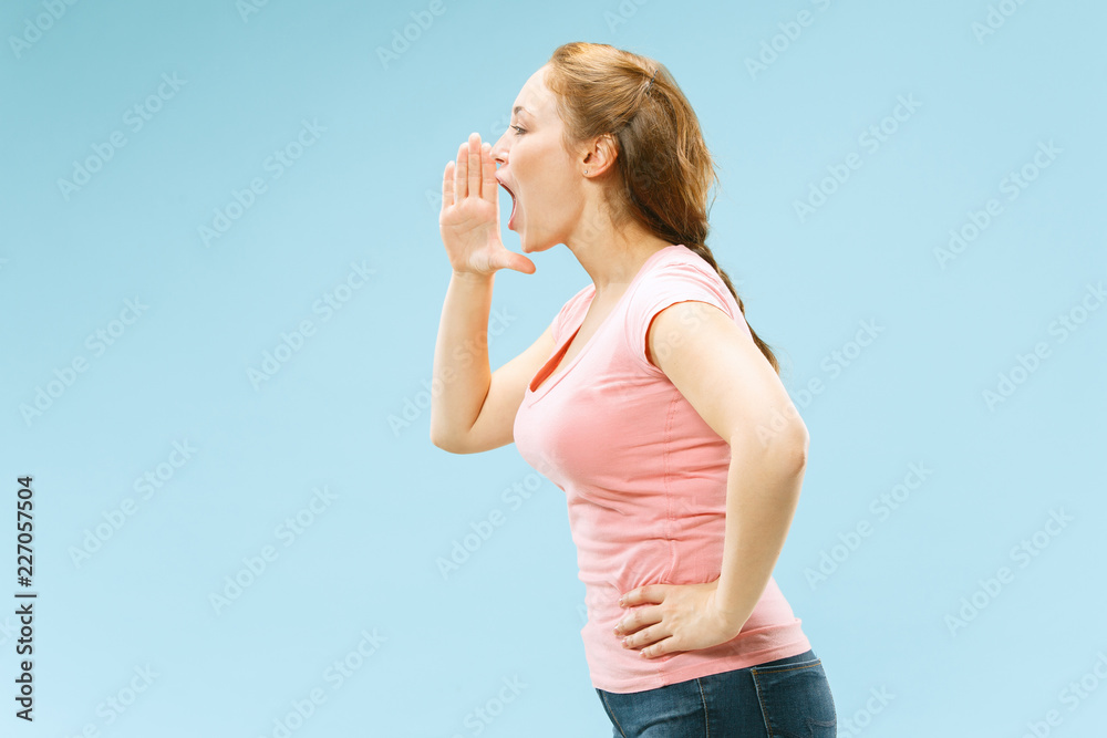 Do not miss. Young casual woman shouting. Shout. Crying emotional woman screaming on blue studio background. Female half-length portrait. Human emotions, facial expression concept. Trendy colors Do not miss. Young casual woman shouting. Shout. Crying emotional woman screaming on blue studio background. Female half-length portrait. Human emotions, facial expression concept. Trendy colors