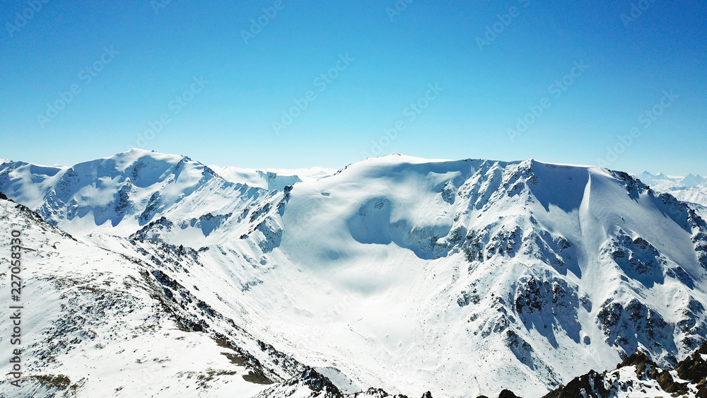 Epic view of snow-capped mountains. Mountain peaks and blue sky. Lots of snow, bright sun, clear sky. Rocks and brown stones are visible. The shadow from the sun falls on the rocks of the mountains. 