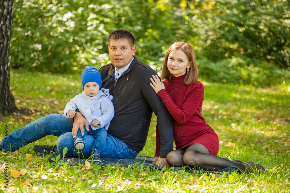 mom, dad and baby are sitting on the grass in the park. Family weekend in the fall