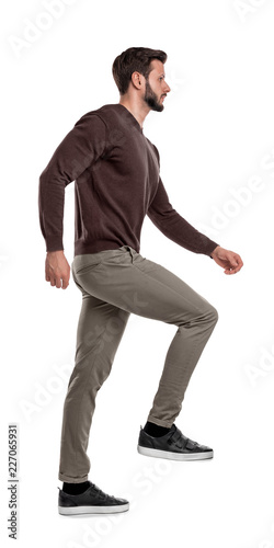 An isolated bearded man in casual wear steps up with one leg in a side view on a white background.