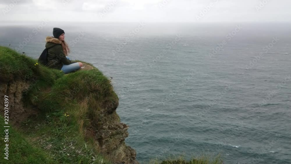 Brave girls sits on the edge of the Cliffs of Moher in Ireland Brave girls sits on the edge of the Cliffs of Moher in Ireland