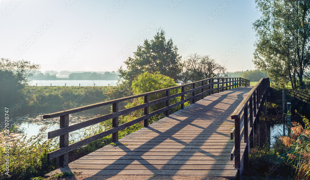 Simple wooden bridge with planks over a narrow Dutch river in the morning sun