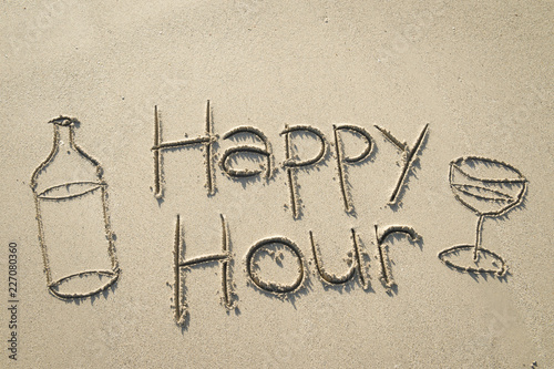 Happy Hour message handwritten in smooth sand with bottle and cocktail glass photo